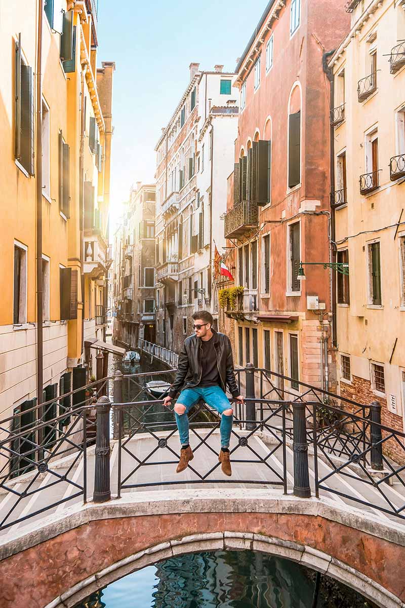 A man sitting on a bridge, overlooking water in an Italian city