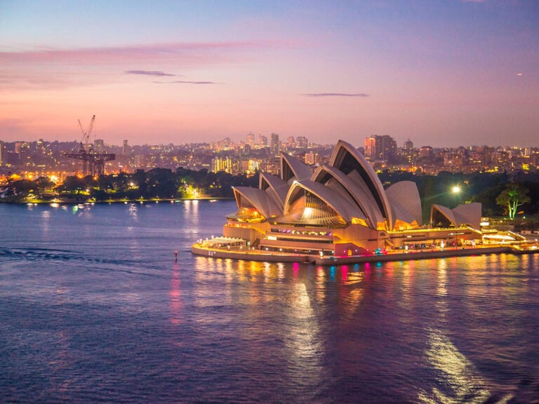 Sydney Opera House in Australia, with sail-like roofs and evening lights reflecting on the water