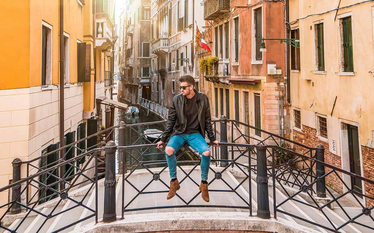 A man sitting on a bridge, overlooking water in an Italian city